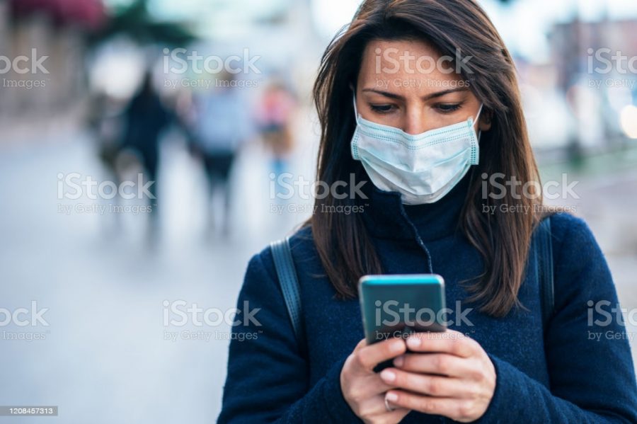 Portrait of young woman on the street wearing  face protective mask to prevent Coronavirus and anti-smog and using smartphone