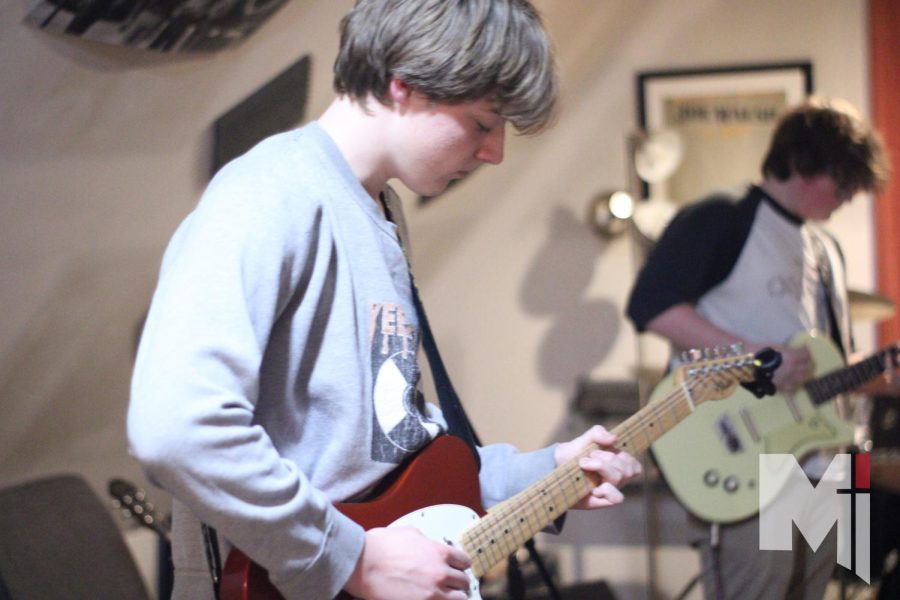 Jamming in his garage-studio with his bandmates, junior Robert Allmon strums on his guitar next to junior Ryder Cahill. The band, named Zero Below, plans on continuing to make music together after they are all out of high school. “Our goal is to make it through college, at least,” Allmon said. 