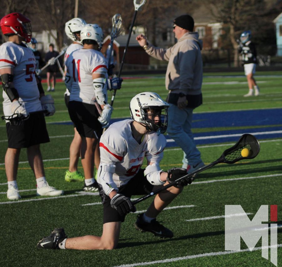 Down on his knee, freshman Nathan Brentano practices drills at lacrosse practice. This is the first year for boys lacrosse at Miege.