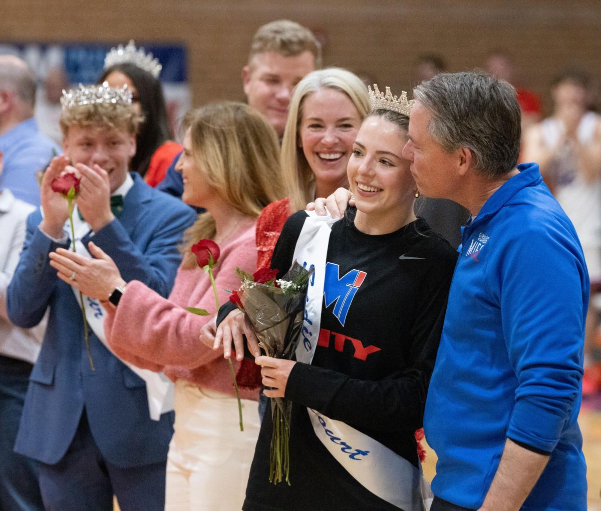 Queen Moment. Senior Mary Grant smiles with her parents as she gets crowned Sadie’s queen at halftime of the boys basketball game on Feb. 13. “I was so surprised that I won,” Grant said. “My parents were really excited and proud of me.”